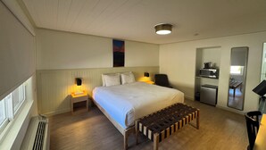 Et hotelværelse med seng, sengeborde, bænk, spejl, mikroovn og køleskab.