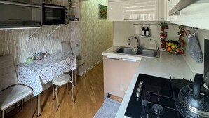 Een compacte keuken met een magnetron, kookplaat, spoelbak en een klein zithoekje met een tafel en stoelen.