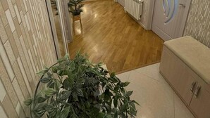 Een hal met houten vloer, witte wanden en een plafond met inbouwverlichting. Aan de rechterkant zijn deuren, links een bankje en in het midden een grote potplant.