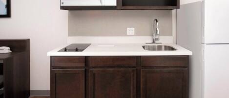 A compact kitchen with a white countertop, dark wooden cabinets, a built-in microwave, and a stainless steel sink.