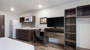 A compact hotel room with a bed, kitchenette, desk, and TV.