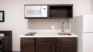 A compact kitchen with a white countertop, dark wooden cabinets, a built-in microwave, and a stainless steel sink. - 3 Queen Studios with Kitchenette – Convenient, Clean, and Close to Attractions (Orlando)
