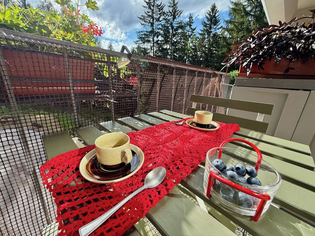 An outdoor dining area with a table set for two, a red tablecloth, and a basket of blueberries.