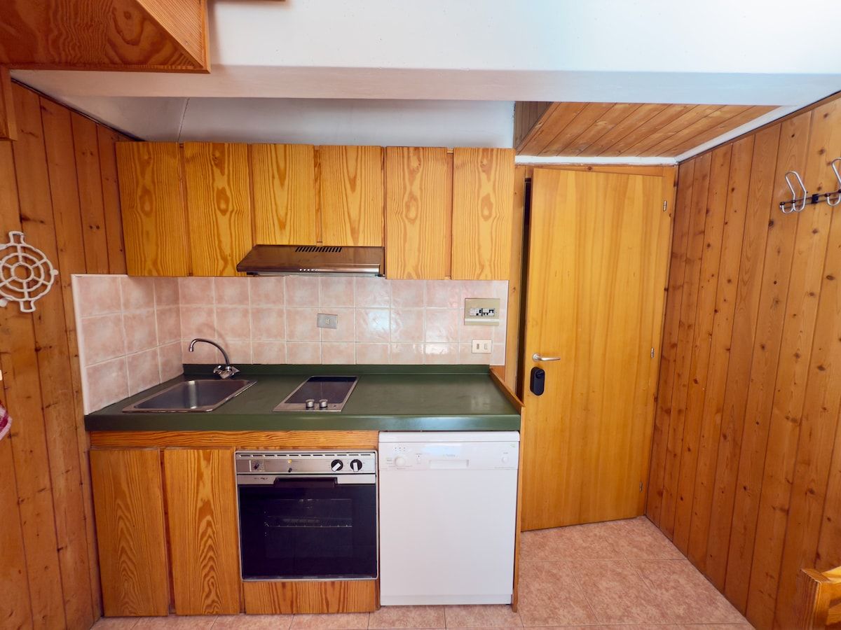 Een kleine keuken met houten kastjes, een spoelbak, een fornuis en een vaatwasser.