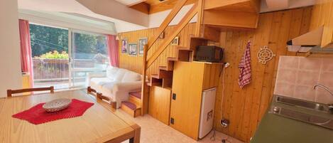 A compact kitchen with wooden cabinets, a dining area with a table and chairs, and a staircase leading to an upper level.