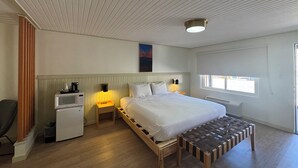 Ein Schlafzimmer mit einem Bett, Nachttischen, einer Bank, einer Mikrowelle und einem Fenster.