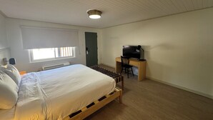 Ein Schlafzimmer mit einem Bett, einem Schreibtisch mit Stuhl, einem Fernseher und einer Tür.