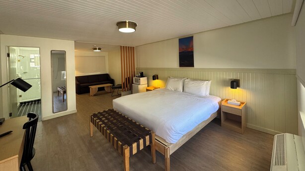 Ein Hotelzimmer mit Bett, Nachttischen, einem Schreibtisch, einem Stuhl, einer Bank, einem Spiegel, einer Couch und einem Bild an der Wand.