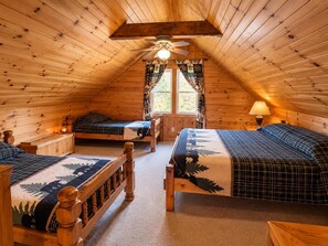 Loft bedroom with wood-paneled walls, triple beds in plaid bedding, a ceiling fan, and nature-themed curtains.