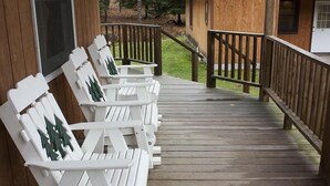 Puinen terassi, jossa on valkoiset Adirondack-tyyliset tuolit ja puinen kaide.