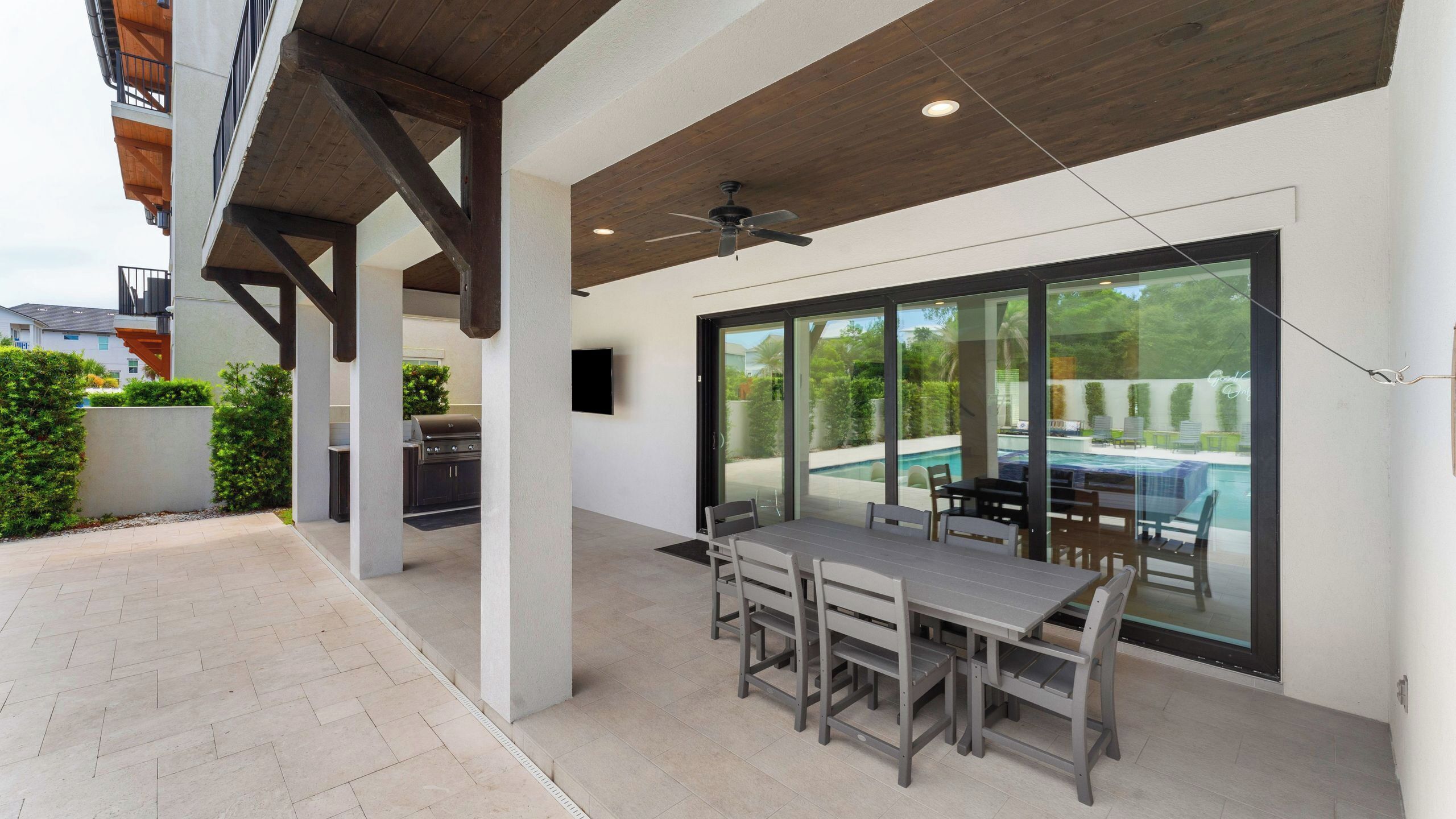 An outdoor patio with a dining table and chairs, a ceiling fan, and a view of a swimming pool.