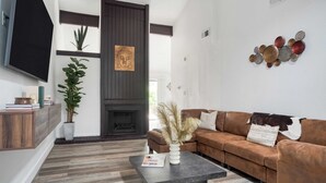 A modern living room with a brown leather sofa, a coffee table, a fireplace, and a wall-mounted TV. - Stylish Retreat, Shared Pool & Yard Near Downtown Fairlawn Lane A by Avantstay (Austin)