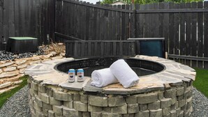A stone fire pit with two bottles and towels. - Stylish Retreat, Shared Pool & Yard Near Downtown Fairlawn Lane A by Avantstay (Austin)