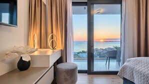 Un dormitorio moderno con un ventanal grande, una cama, un sillón y una mesita con adornos.