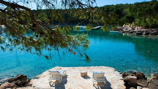 A stone deck with two lounge chairs overlooking a clear blue sea, with rocky terrain and trees in the background. - Villa Island Star with Pool (Milna)