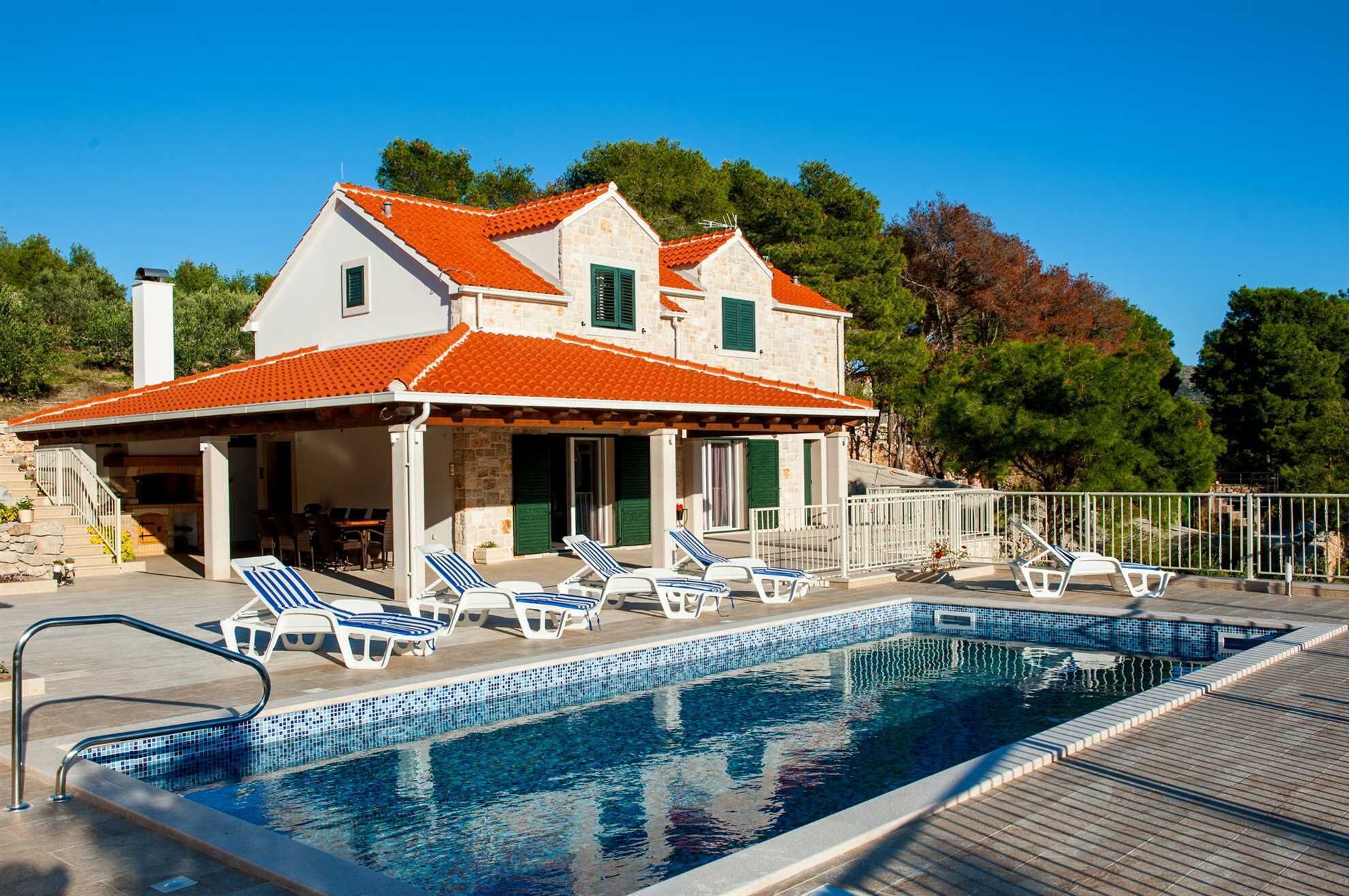 A two-story house with a swimming pool, outdoor seating, and a stone facade.