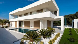 Una casa moderna de dos pisos amb piscina, un balcó i un jardí ben cuidat.