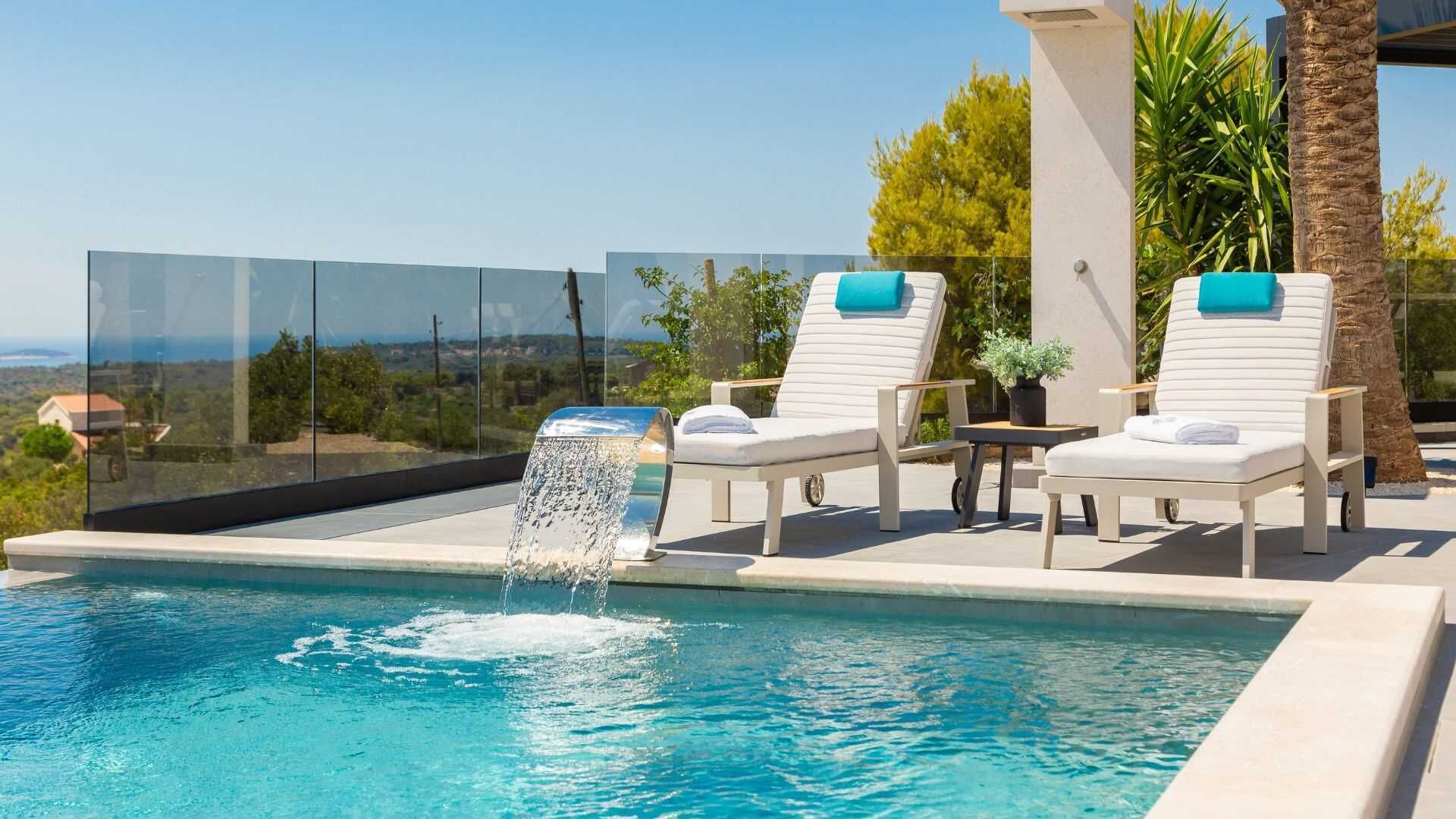 A pool with a water feature, two lounge chairs, and a view of the landscape.