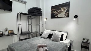 A modern bedroom with a bed, a mounted air conditioner, a wall-mounted TV, a painting, and a small bedside table. - Cozy apartment in the heart of Rio de Janeiro - Lapa (Centro Rio de Janeiro)