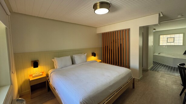 A bedroom with a wooden bed, nightstands, a wall-mounted light, and a view of a bathroom. - Non-Smoking King With Jacuzzi - NKJ (Manitou Springs)