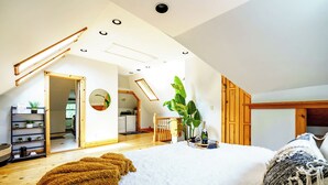 Ein geräumiges Schlafzimmer mit einem großen Bett, einer Holztreppe und einer Küche im Hintergrund.
