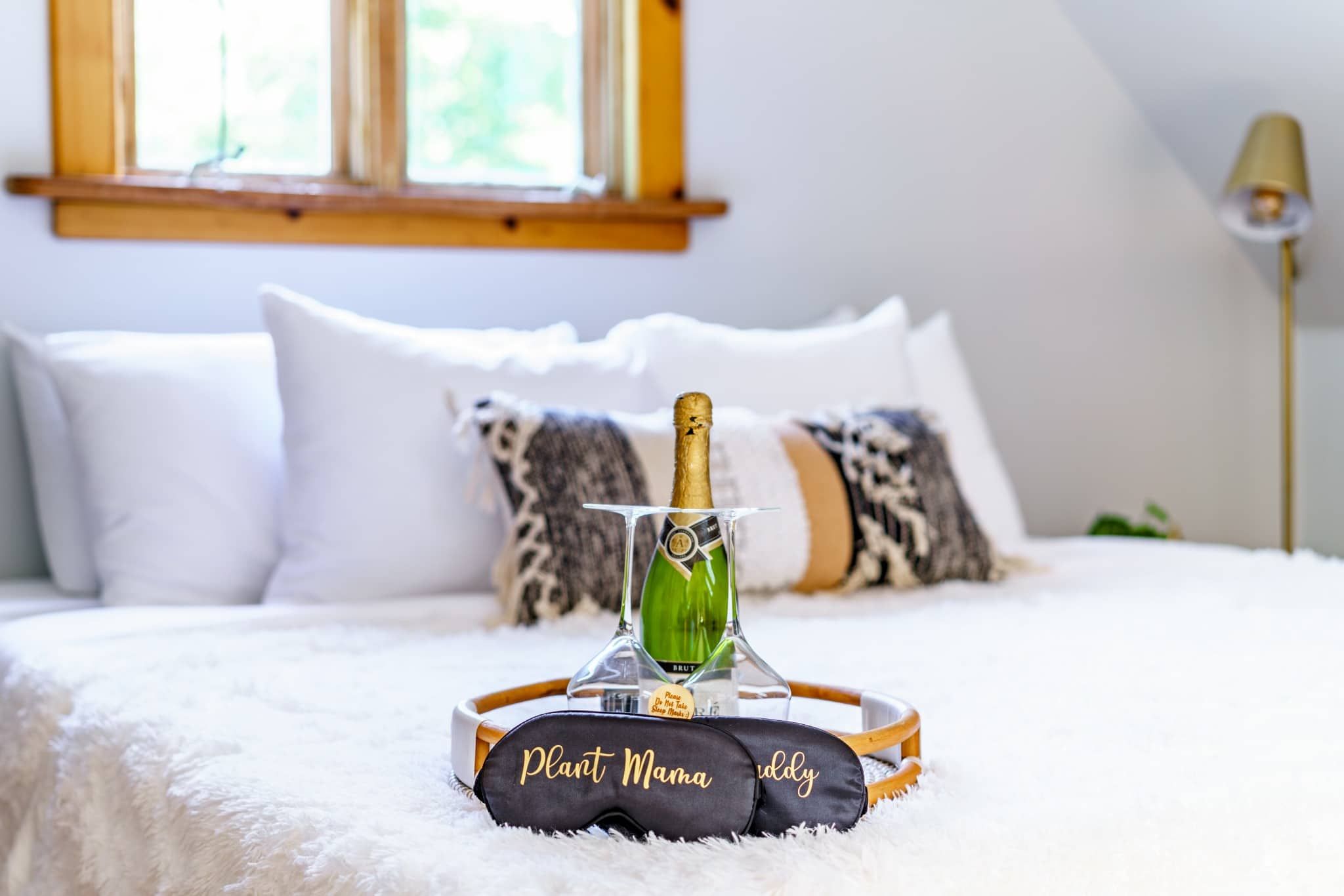 A bed with a bottle of champagne, a tray with a name tag, and pillows.