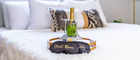 A bed with a bottle of champagne, a tray with a name tag, and pillows.