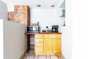 A compact kitchen with a brick wall, a microwave, a coffee maker, and a small plant on the counter. - Short North & Downtown & OSU | Near High Street | Free Parking | 5,800+ Reviews (Columbus)