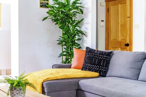 A living room with a grey sofa, a yellow throw blanket, and a potted plant. - Short North & Downtown & OSU | Near High Street | Free Parking | 5,800+ Reviews (Columbus)