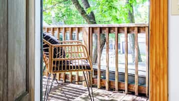 A wooden deck with a wicker chair and a view of green trees through a glass door.