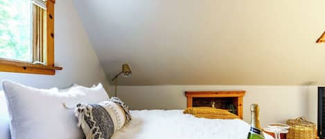 Un dormitorio con cama, almohadas, una lámpara, chimenea y una botella de champán.