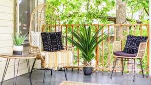 Eine Veranda mit zwei Korbstühlen, einem kleinen Tisch und einem Blumentopf.