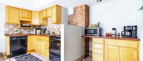 Une cuisine compacte avec des meubles en bois, un mur en briques, un four à micro-ondes, une machine à café et un lave-vaisselle.