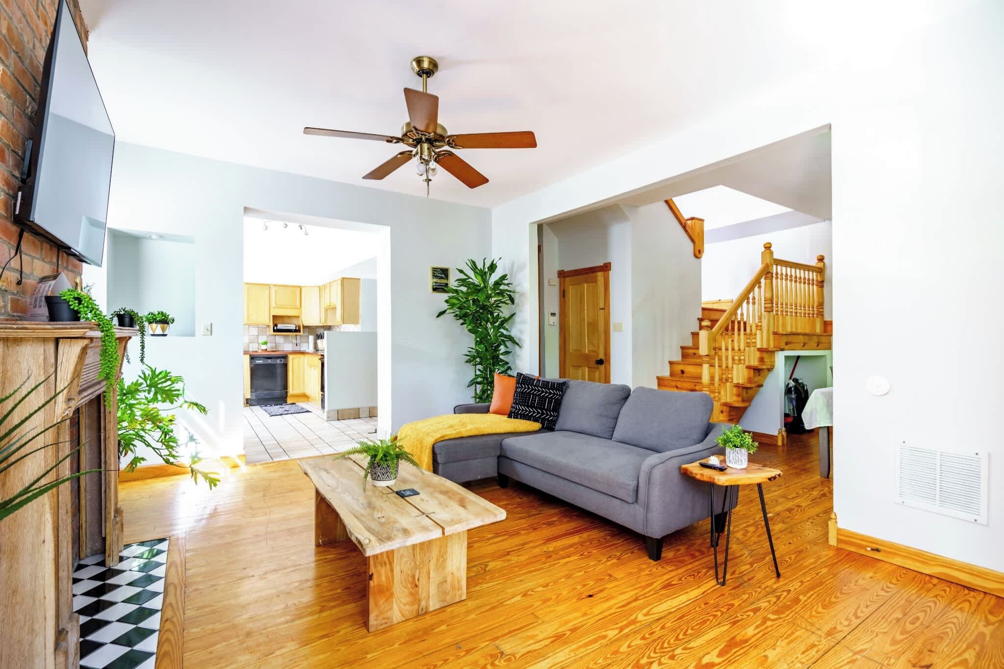 Un salon moderne avec un plancher en bois, un canapé gris, une table basse en bois et un ventilateur de plafond.