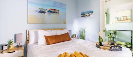 A bedroom with a bed, a nightstand, a lamp, a bottle of champagne, and a small plant.
