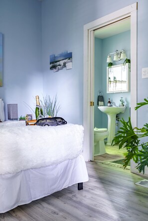 A bedroom with a bed, a bedside table with a bottle, and a plant.