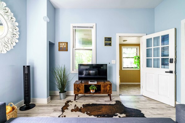 A living room with a television on a wooden stand, a cowhide rug, a potted plant, and a decorative mirror. - Short North & Downtown & OSU | Near High Street | Free Parking | 5,800+ Reviews (Columbus)