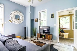A living room with a sofa, a television on a wooden stand, a decorative mirror, and a plant. - Short North & Downtown & OSU | Near High Street | Free Parking | 5,800+ Reviews (Columbus)