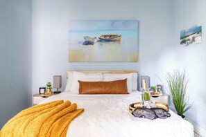 Een slaapkamer met een bed, een nachtkastje, een lamp, een aan de muur hangend schilderij en een pot met een plant.