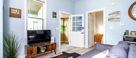 Un salon avec un téléviseur à écran plat posé sur un meuble en bois, un tapis en peau de vache, un canapé gris et un ventilateur de plafond.
