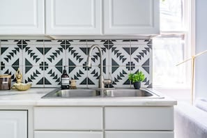 Eine Küche mit weißen Schränken, einem Edelstahl-Spülbecken und einer geometrisch gemusterten Spritzschutzwand.