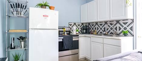 A modern kitchen with white cabinets, a stainless steel refrigerator, and a microwave. There is a wooden countertop with a coffee maker and a plant.