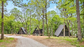 A gravel path leading to three dark-colored cabins surrounded by trees.