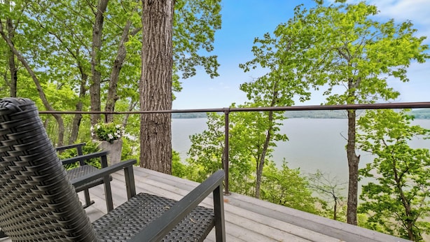 A wooden deck with a metal railing overlooking a lake, surrounded by trees.