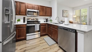 Una cocina moderna con electrodomésticos de acero inoxidable, armarios de madera y encimera blanca.