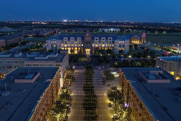 A large building with multiple floors, a central courtyard with trees, and a sports field in the background.