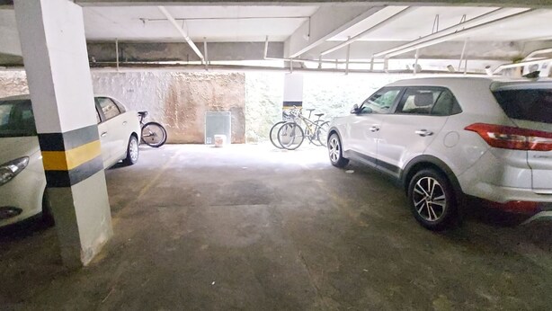 A parking garage with two cars parked, a bicycle, and a concrete pillar. - CONAZ0100 - Edifício Larissa (Salvador)