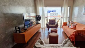 A living room with a sofa, a chair, a TV on a stand, and a fan. - CONAZ0100 - Edifício Larissa (Salvador)