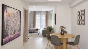 A modern living room with a dining area, featuring a large abstract painting, a round wooden table, and grey upholstered chairs.