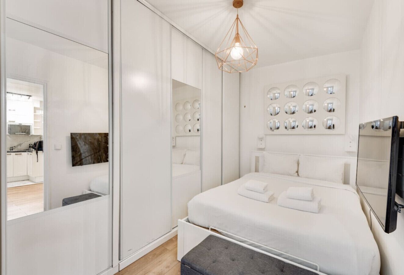 Un dormitorio moderno con una cama grande, una mesita de noche, un espejo y una lámpara de pared.